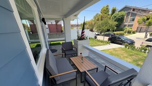 A covered patio with outdoor seating, a flag, and a view of the neighborhood.