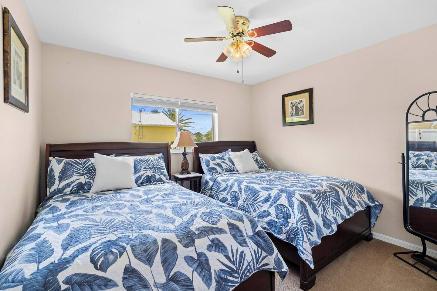 A bedroom with two beds, a ceiling fan, a window with a view, and a mirror.