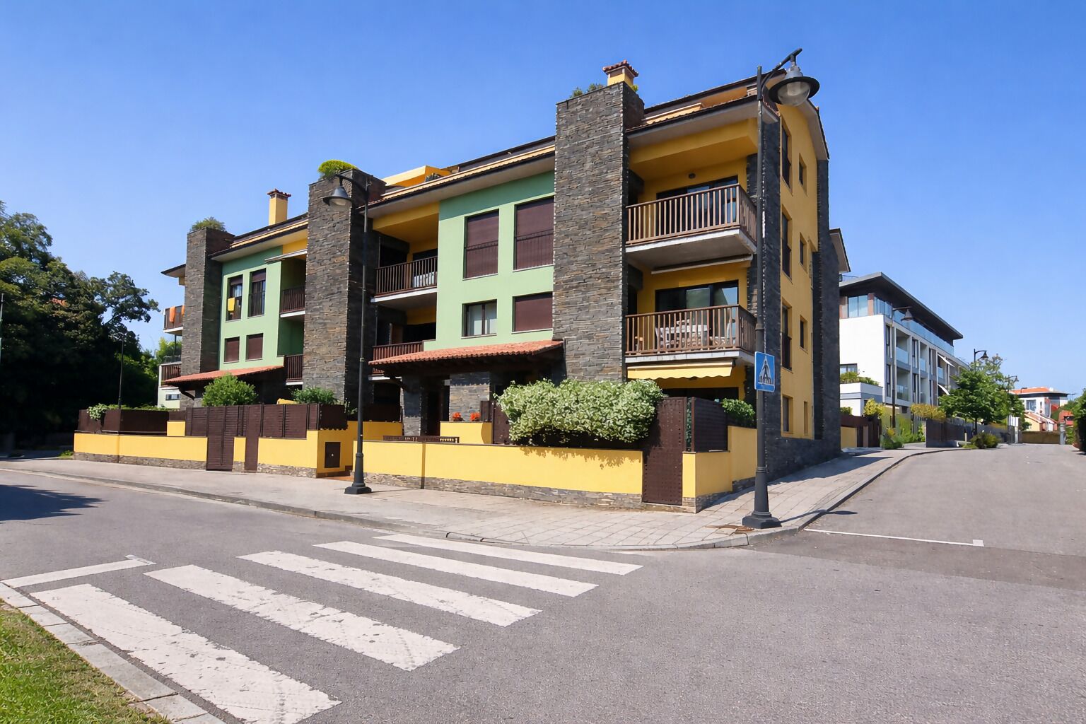A multi-story building with balconies, a pedestrian crossing, and a clear sky.