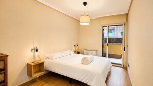 A bedroom with a bed, bedside lamps, a wooden nightstand, a radiator, and a view through a glass door.