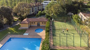 A swimming pool, tennis court, and a building with a tiled roof.