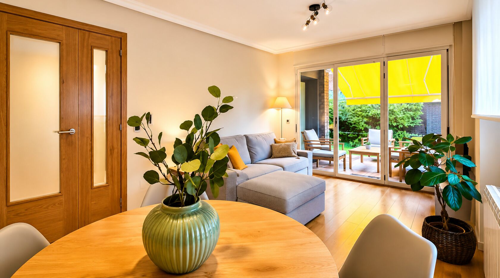 Una sala de estar moderna con una mesa de comedor de madera, un sofá y un amplio ventanal corredera que da a un espacio exterior.