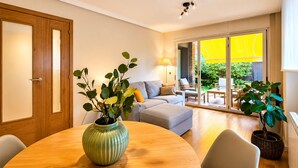 A modern living room with a wooden dining table, a sofa, and a large sliding glass door leading to an outdoor area.