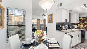 A dining area with a round table set for four, a kitchen with white cabinets, and a decorative flower arrangement on the counter. - Stylish Chandler Stay - 2 King Beds, 2 Baths! (Chandler)