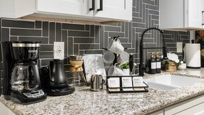 A kitchen with a black and white tiled backsplash, a coffee maker, a kettle, and a coffee station with cups and a sign. - Stylish Chandler Stay - 2 King Beds, 2 Baths! (Chandler)