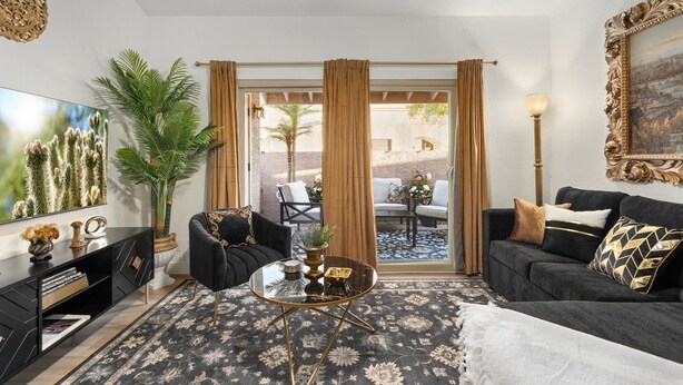 A modern living room with a black sofa, a glass coffee table, and a large TV. There is a potted plant and a painting on the wall. - Stylish Chandler Stay - 2 King Beds, 2 Baths! (Chandler)