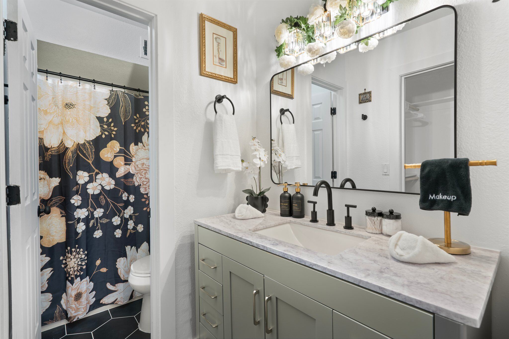 Casa de banho com cortina de chuveiro estampada com flores, pia com torneira dourada e toucador com espelho.