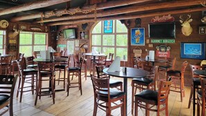 Un intérieur rustique avec des poutres en bois, de nombreuses tables et chaises, et divers éléments de décoration murale, notamment des panneaux et une tête de cerf fixée au mur.