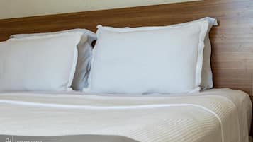 Una cama bien tendida con ropa de cama y almohadas blancas, cabecera de madera y el logotipo de Andrade Hotels.
