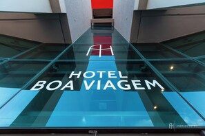 Une entrée d’hôtel moderne avec un sol en verre et un mur d’accent rouge.