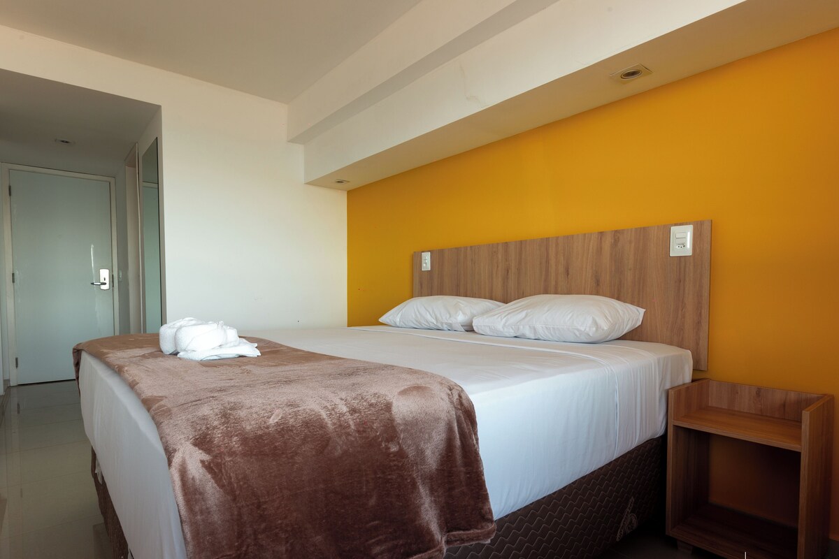 Habitació d'hotel amb un llit, un capçal de fusta, una manta marró i una tovallola blanca.