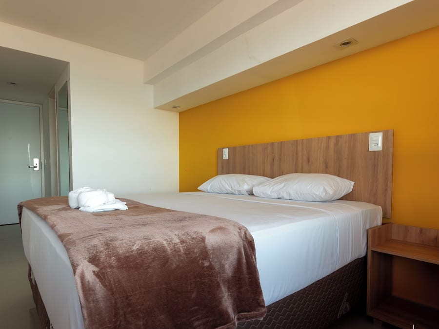 Una habitación de hotel con una cama, cabecera de madera, manta marrón y toalla blanca.