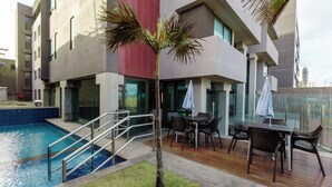 Et moderne hotel med swimmingpool, udendørs siddepladser og en palme.