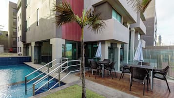 Un hotel moderno con piscina, zona de estar exterior y una palmera.