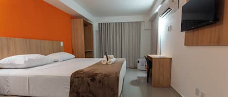 Una habitación de hotel con cama, escritorio, televisor y aire acondicionado.