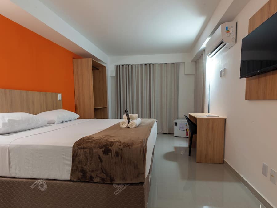 A hotel room with a bed, a desk, a television, and an air conditioning unit.