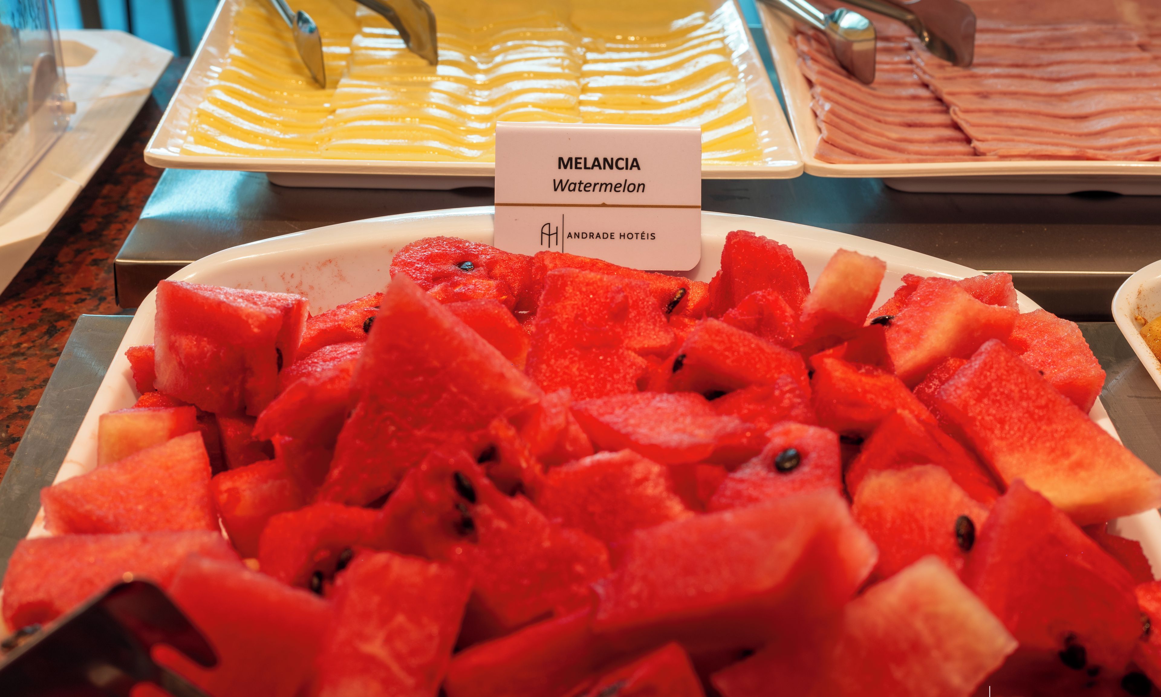 Un bufé con una sección de sandía identificada como "Melancia Watermelon" en Andrade Hotels.