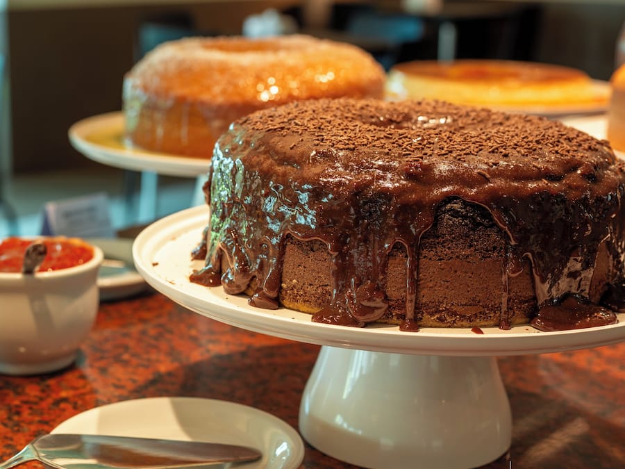 A chocolate cake with chocolate drizzle on a white cake stand.