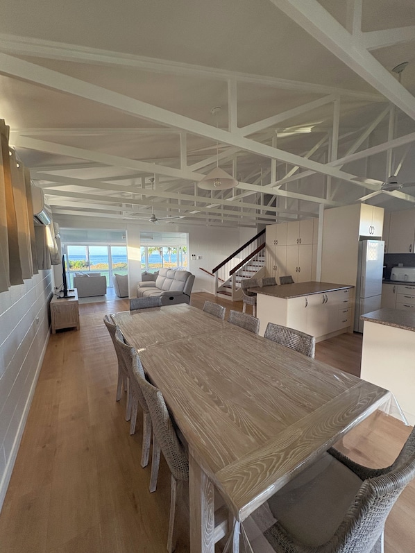 A spacious kitchen with a large wooden table and wicker chairs, a built-in oven, and a view of the ocean. - Luxury @ Lucinda (Lucinda)