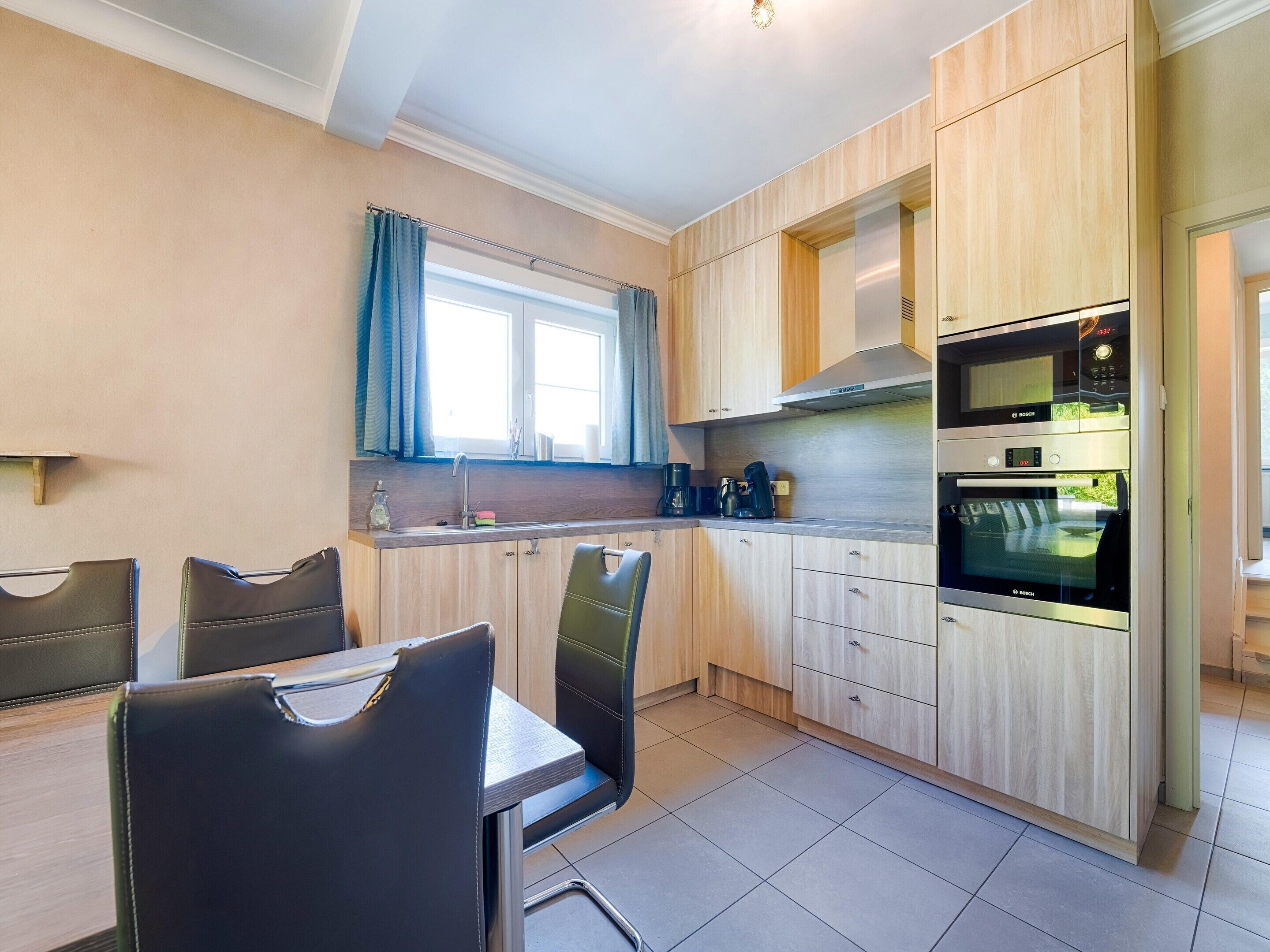 A modern kitchen with wooden cabinets, a Bosch oven, and a dining area with two chairs.