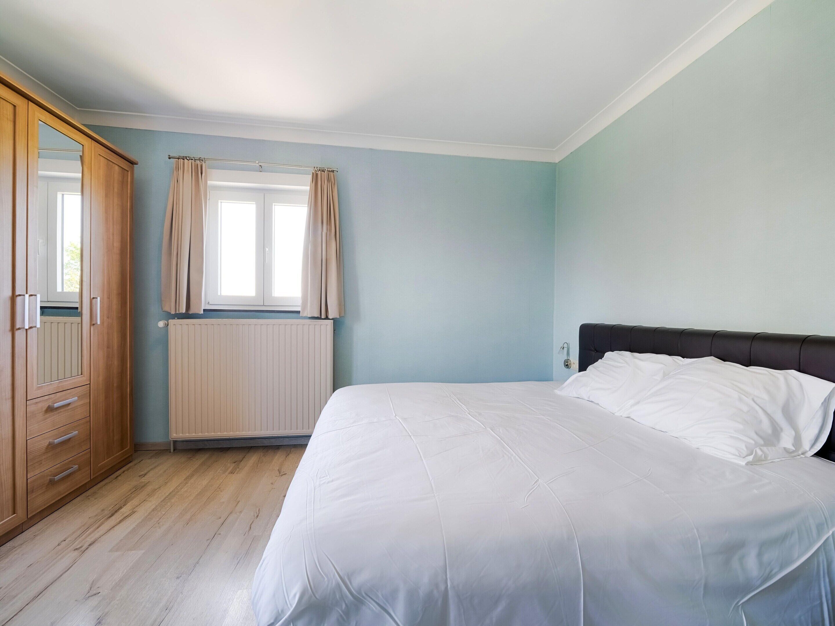 A bedroom with a bed, wooden wardrobe, and a window with curtains.