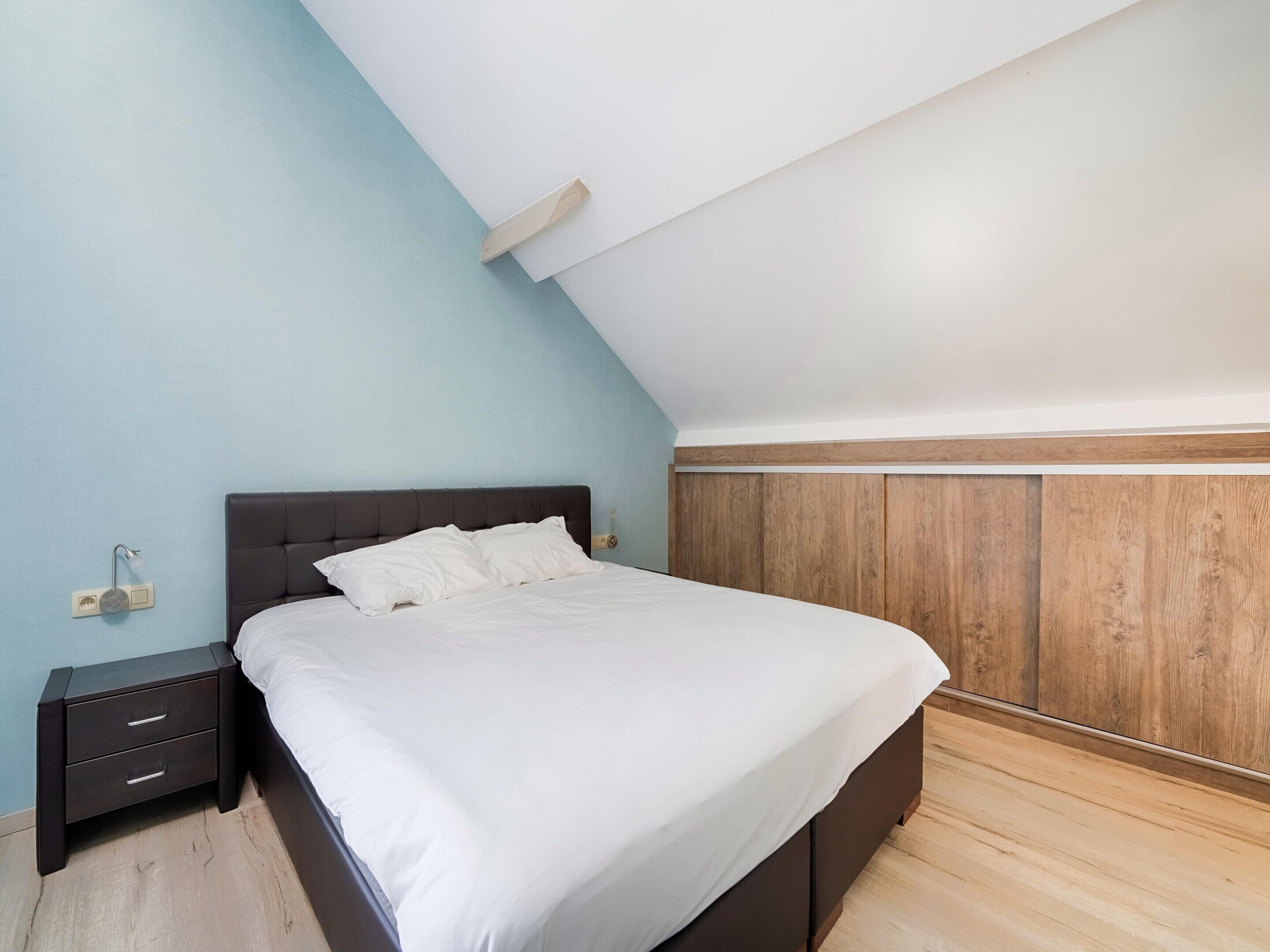 Een slaapkamer met een bed, nachtkastje en een wand van houten panelen.