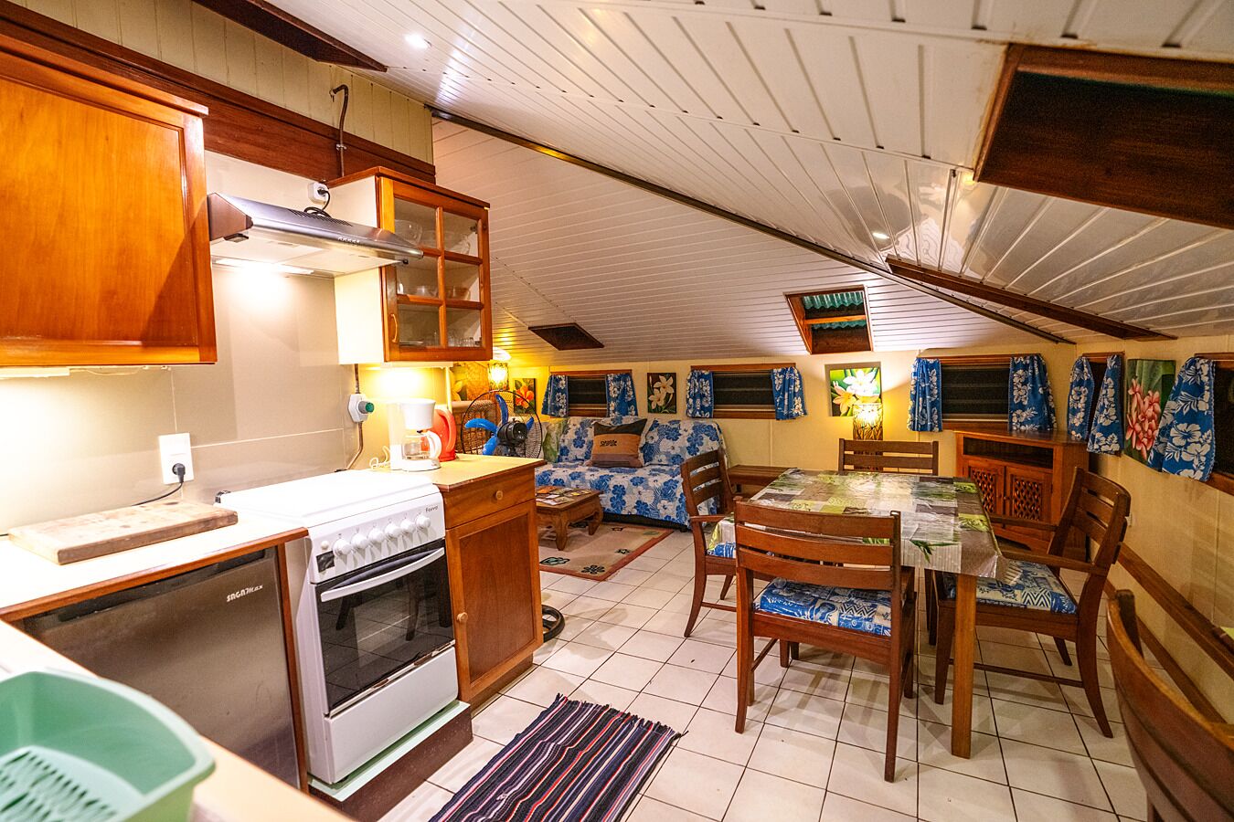 A compact kitchen with a stove, oven, and sink, a dining area with a table and chairs, and a living space with a sofa and curtains.