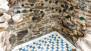 Una habitación con paredes de piedra, suelo de cuadros, vigas de madera y botellas de vidrio colgando.