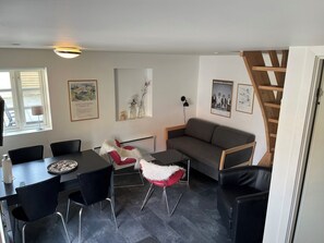 Una sala de estar moderna con un sofá, una mesa de comedor con sillas, una escalera y obras de arte en las paredes.