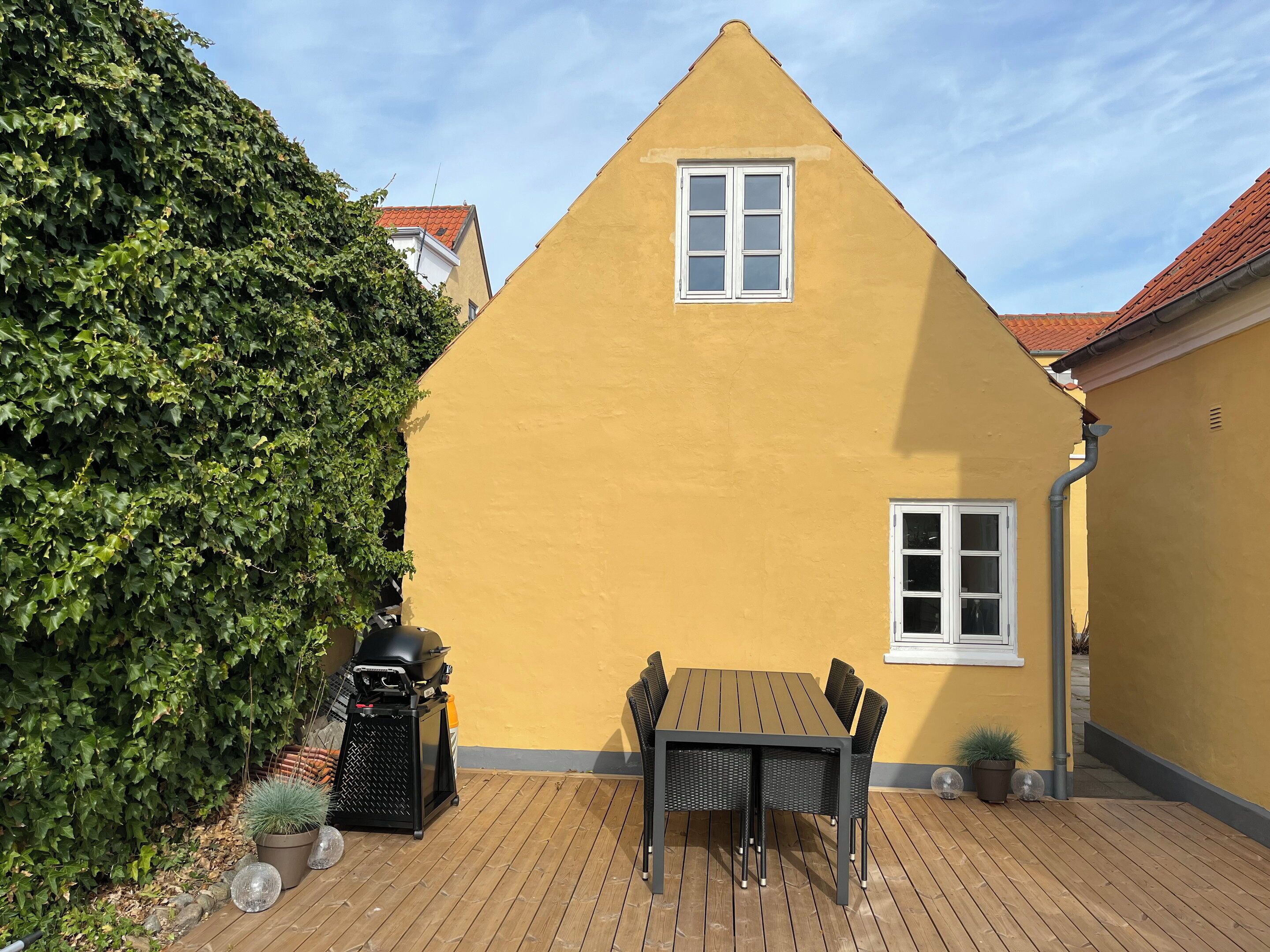 Un edificio amarillo con techo triangular, una ventana y una mesa con sillas al frente.