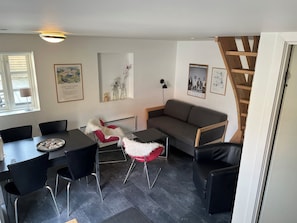 Ein modernes Wohnzimmer mit Esstisch, roten und weißen Stühlen, einem grauen Sofa und einer Treppe.