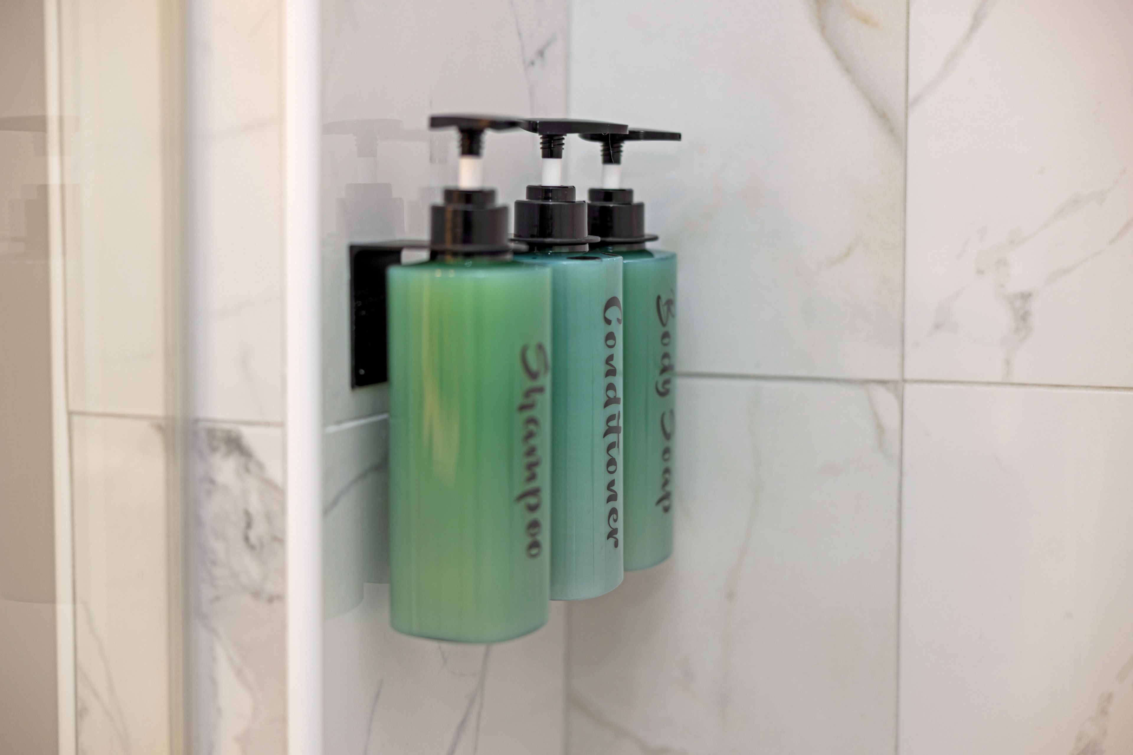 Ein Badezimmer mit einem an der Wand montierten Spender, der drei Shampooflaschen enthält.