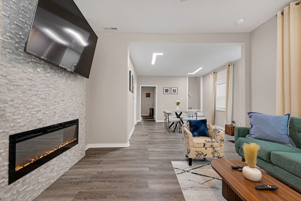 A modern living room with a fireplace, a flat-screen TV, a dining area, and a green sofa.