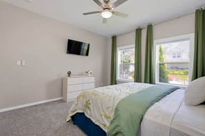 A bedroom with a bed, a dresser, a television on the wall, and a window with curtains.