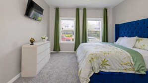 A bedroom with a bed, a dresser, a television mounted on the wall, and a ceiling fan.