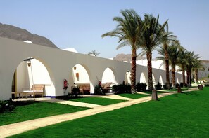 A hotel corridor with white arches, palm trees, and a clear sky.