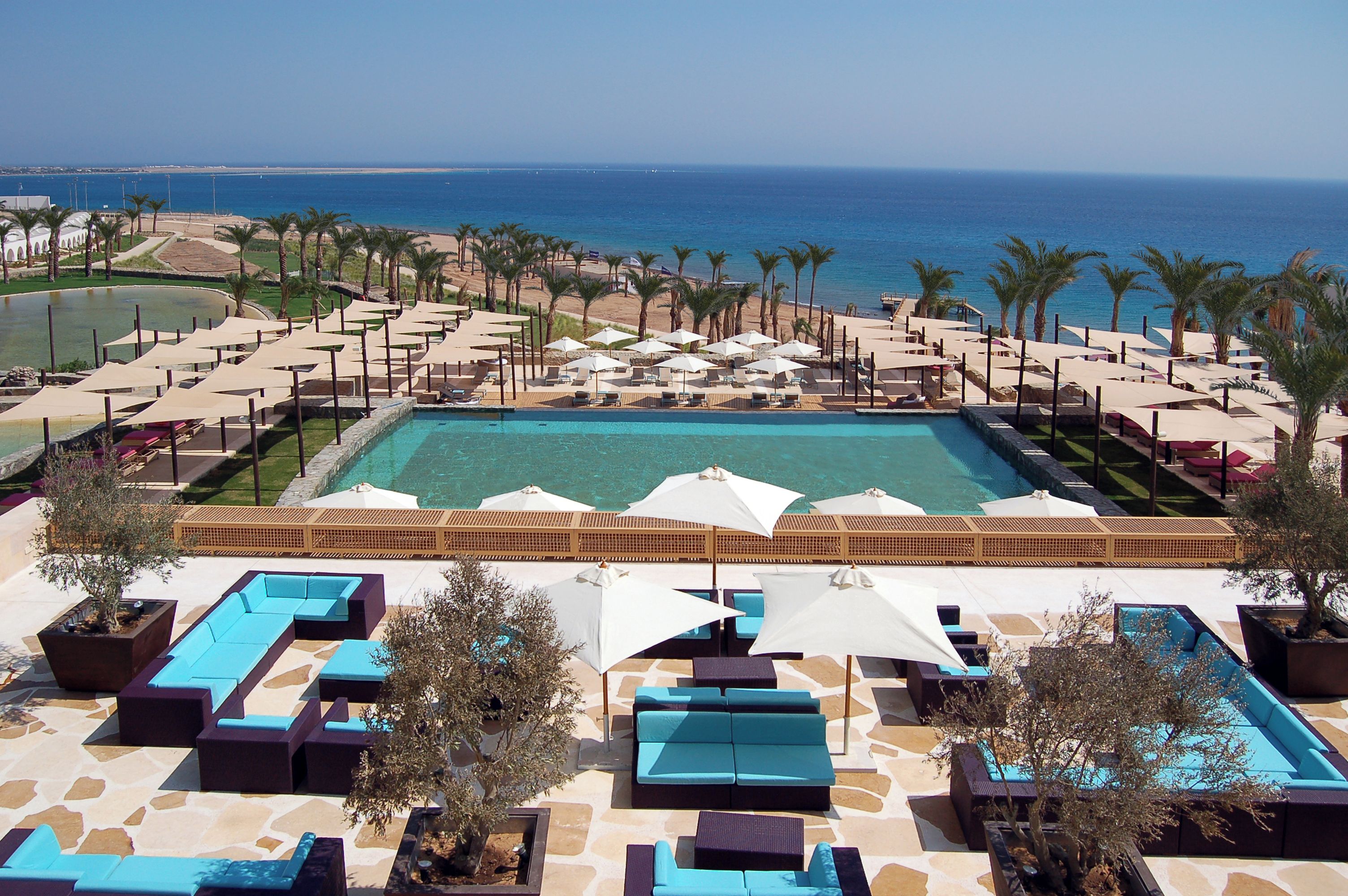 A poolside area with lounge chairs and umbrellas, a large pool, and a view of the ocean.