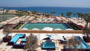 A poolside area with lounge chairs and umbrellas, a large pool, and a view of the ocean.