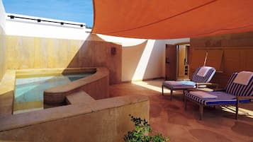 A sunlit outdoor area with a hot tub, lounge chairs, and a wooden deck.