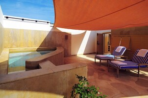 A sunlit outdoor area with a hot tub, lounge chairs, and a wooden deck.