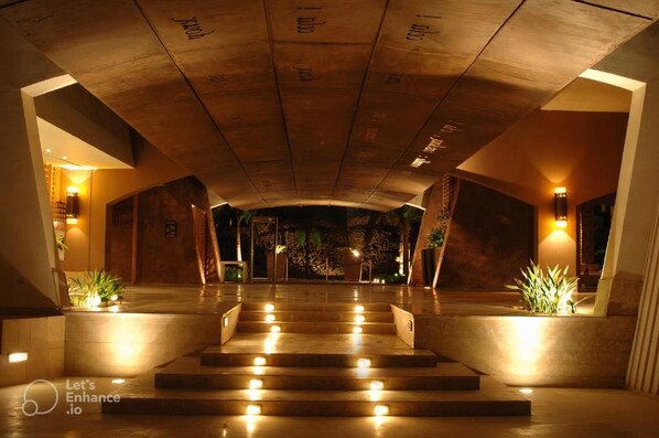 Un vestíbulo de hotel con una escalera monumental, iluminación cálida y diseño moderno.
