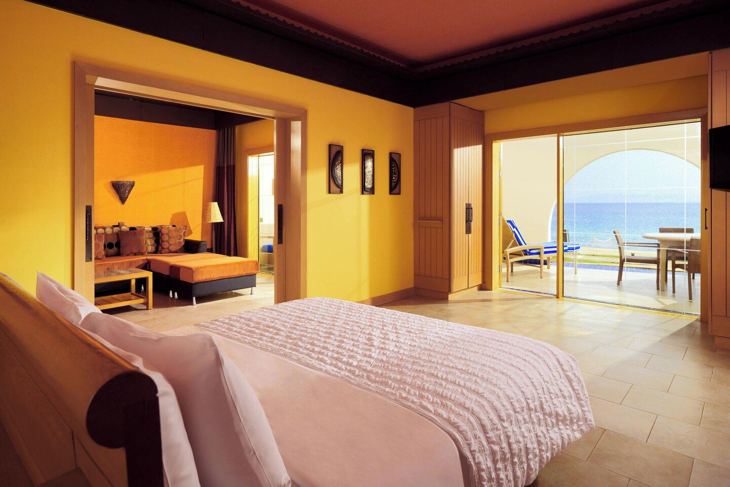 A hotel room with a bed, a seating area with a sofa and a table, and a balcony with a view of the sea.