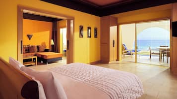 Quarto de hotel com cama, área de estar com sofá e mesa, e varanda com vista para o mar.