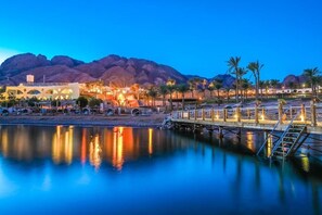 A waterfront hotel with a pool, palm trees, and a mountain backdrop. - Retac Qunay Dahab (Dahab)