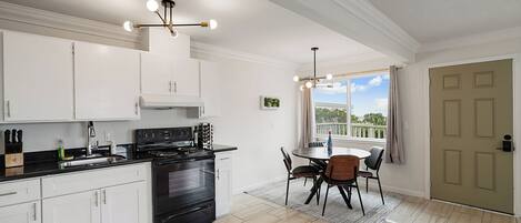 A modern kitchen with white cabinets, a black stove, and a dining area with a round table and chairs.