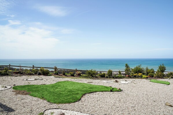 A landscaped outdoor area with a view of the sea, a wooden fence, and various plants.