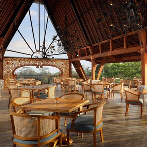 An outdoor dining area with wooden tables and chairs, a decorative ceiling, and a view of greenery. - Abisena Wellness & Resort Ubud Adult Only (Tegallalang)