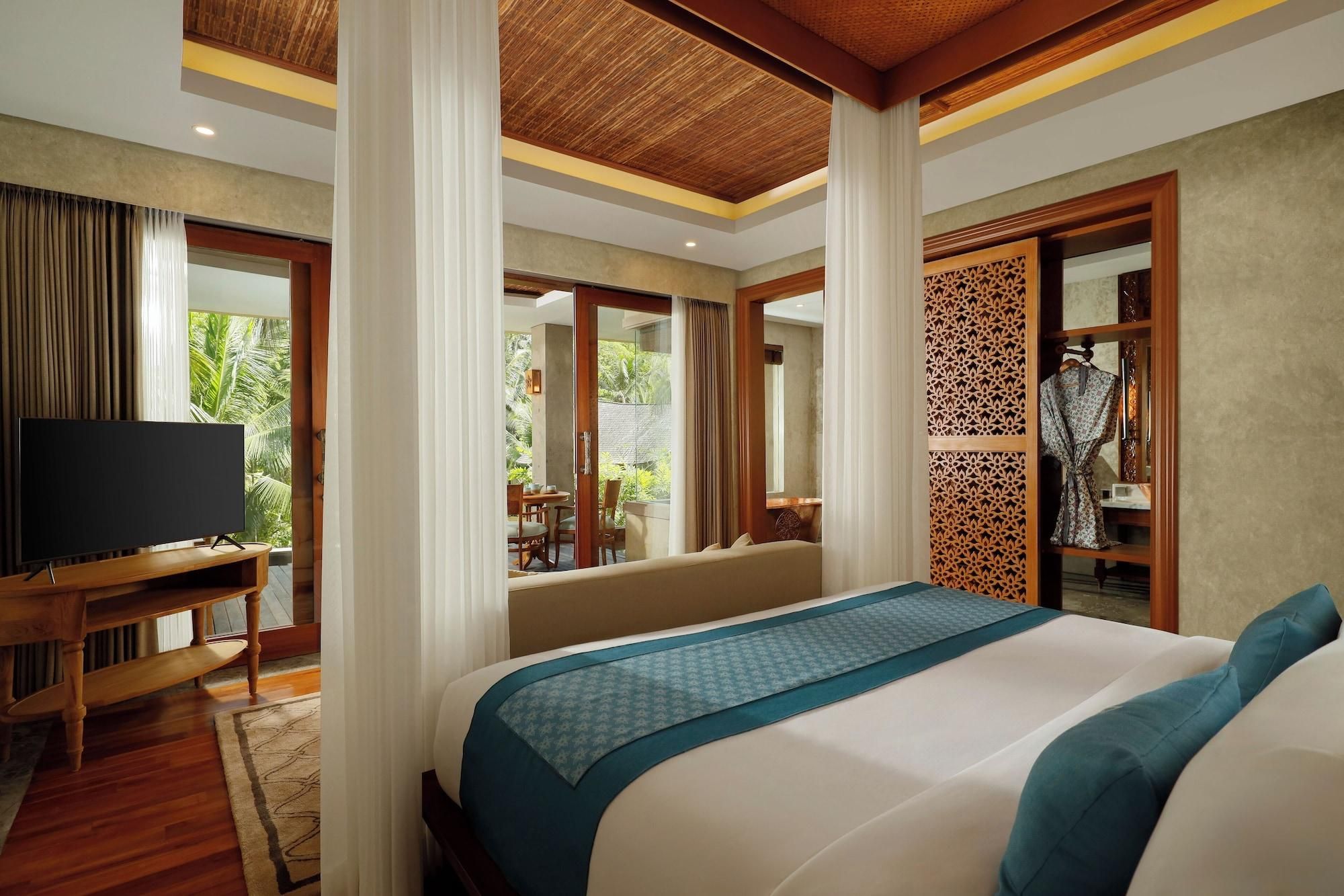 A hotel room with a large bed, a TV, a wooden desk, and a view of the outdoors.