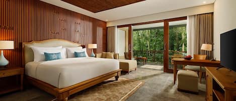 A hotel room with a large bed, a desk, a TV, and a balcony with a view of greenery.
