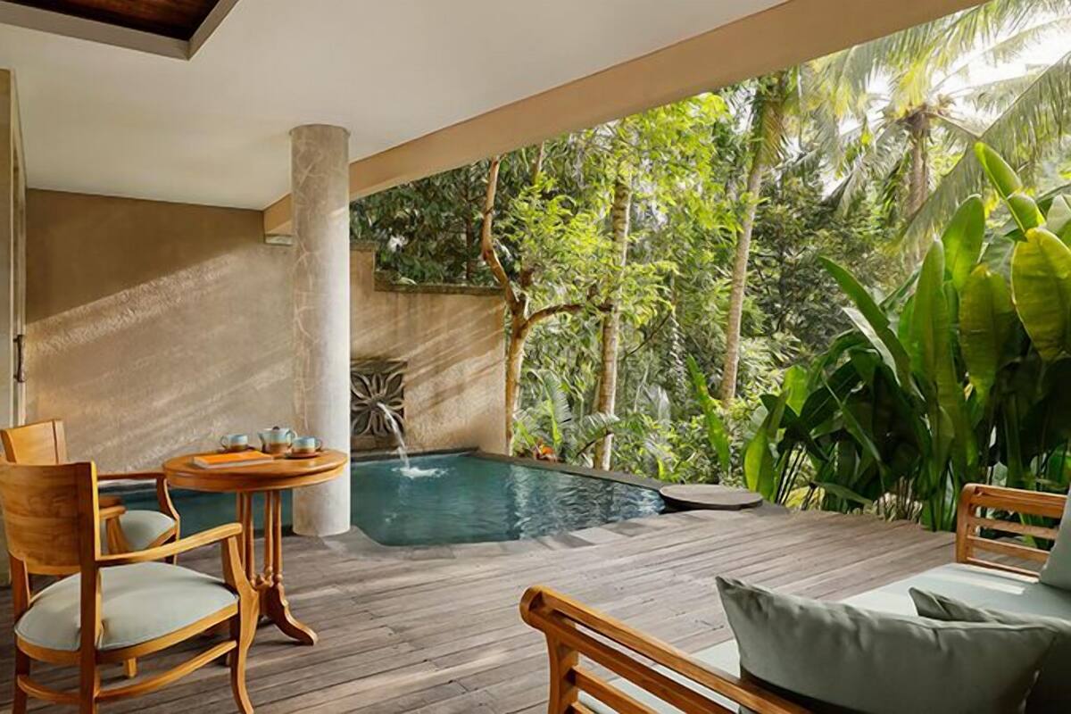 A wooden deck with a hot tub, chairs, and a view of lush greenery.
